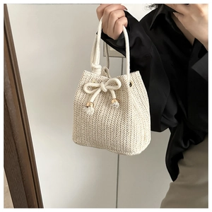 Close-up of cream woven bucket bag with white rope handle and bow detail for summer