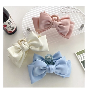 Detailed view of oversized satin bow hair claws in pink, cream, and sky blue colors