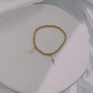 Close-up of gold beaded bracelet with a white pearl and lightning bolt charm detail