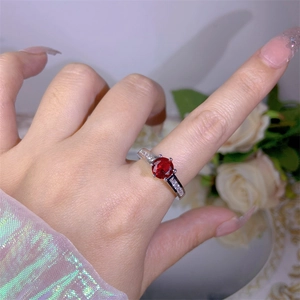 Close-up of a silver ring featuring a round red gemstone and cubic zirconia on the band