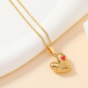 Detail of gold heart pendant with textured surface and small red heart inlay detail