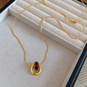 Detailed macro view of a gold-plated snake chain necklace with a red stone U-shaped pendant