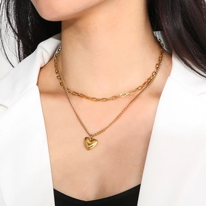 Close-up of golden double-layer necklace with heart pendant on a model in white blazer