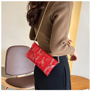 Model wearing a red envelope clutch bag with gold chain strap and stylish pattern