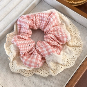 Detailed view of a pink plaid scrunchie with beige lace trim in a wooden tray