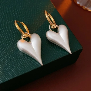 Detail of matte silver heart pendant with brushed texture on gold hoop earring