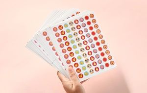 Close-up of a hand holding a stack of colorful round reward stickers with cute cartoon patterns