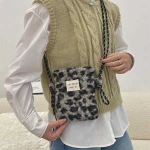Close-up of leopard print plush crossbody bag with logo label and thin cord strap