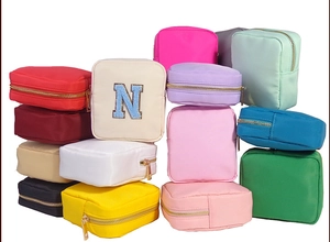 Stacked collection of colorful nylon pouch bags with embroidered N detail on white background