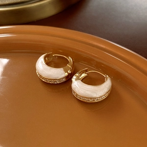 Detail of gold hoop earrings with white enamel finish and shimmering zircon accents