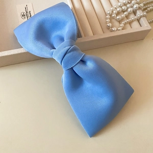 Close-up of light blue satin bow hair clip on a beige tray with pearl necklace