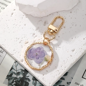 Detail of floral resin keychain with real purple dried flowers and gold metal frame