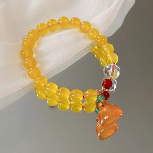 Detailansicht eines gelben Perlenarmbandes mit orangefarbenem Lotusanhänger auf Seide