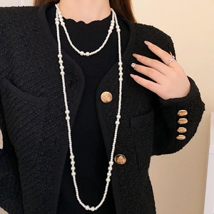 Dettaglio di una collana di perle bianche a più strati abbinata a una giacca in tweed nero
