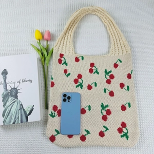 Detailed close-up of beige knitted tote bag featuring a vibrant red cherry pattern