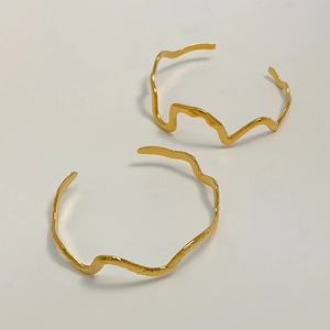 Detail shot of wavy gold-plated stainless steel bangles with liquid texture finish