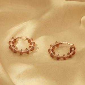 Detail view of rose gold C-shaped earrings with spiral metal coil texture on silk