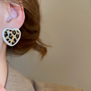 Close-up of heart-shaped leopard print earrings with a white border on a model