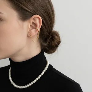 Gold tassel chain ear cuff with round plate detail worn by a model on a dark background