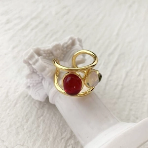 Detail of a gold double-band ring featuring red, white, and green gemstones on a statue