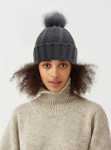 Close-up of a grey knit beanie with a fluffy fur pom-pom and thick ribbed texture