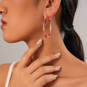 Golden hoop earrings with red enamel stripes and textured design shown on a model
