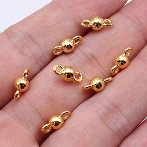 Detail einer Hand mit goldenen kugelförmigen Verbindern für DIY-Schmuckherstellung