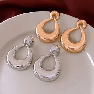 Glossy gold and silver geometric water-drop earrings in a ceramic dish on red fabric