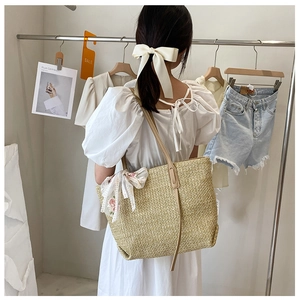 Detail of beige straw tote bag with lace bow accessory worn by a model in boutique