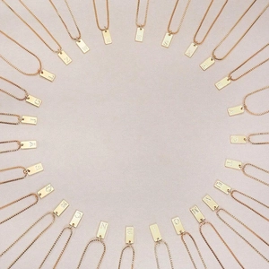 Detailed overhead view of 26 gold square initial pendants on stainless steel box chains