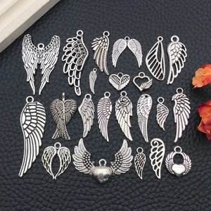 Variety of antique silver angel wing charms displayed on black leather for DIY jewelry