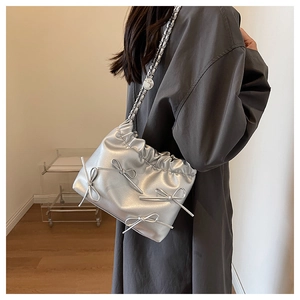 Detail of silver metallic pleated bucket bag with bow and chain strap on shoulder