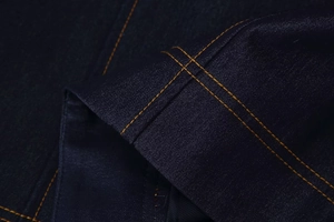 Détail du tissu denim bleu foncé avec coutures contrastées jaunes sur la veste