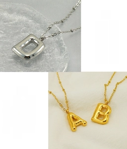 Macro detail of puffy balloon style alphabet charms in polished steel and gold finish