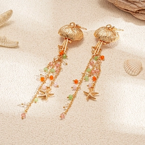 Detail of jellyfish tassel earrings with colorful beads and starfish on sand background