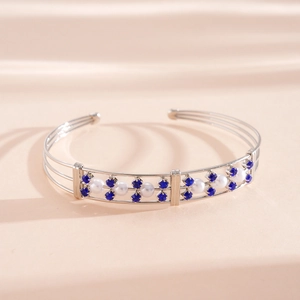 Detailansicht eines silbernen dreilagigen Armreifs mit blauen Strasssteinen und Perlen.
