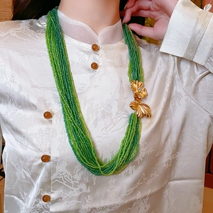 Detail of multi-strand green beaded necklace with golden floral accents on model's neck
