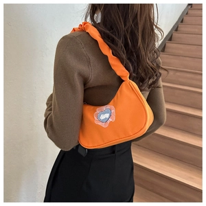 Detail of orange nylon underarm bag with pleated strap and white rabbit heart patch