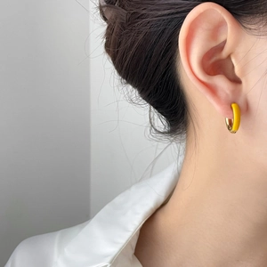 Close-up of yellow and gold enamel twisted hoop earring worn on a model's ear