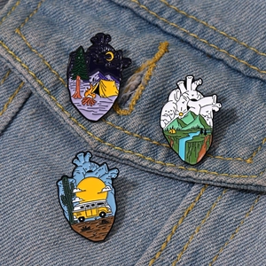 Creative anatomical heart enamel pins with landscape scenes on a blue denim jacket