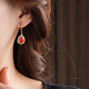 Detail of earring with teardrop red crystal and tassel on model in gold finish