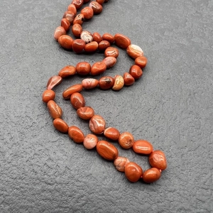 Macro detail of irregular reddish-brown natural stone beads on a stainless steel necklace