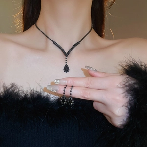 Close-up of black teardrop earrings and V-shaped necklace set on a fashion model