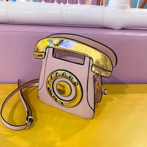 Close-up of pink rotary phone crossbody bag with gold dial detail on a colorful background