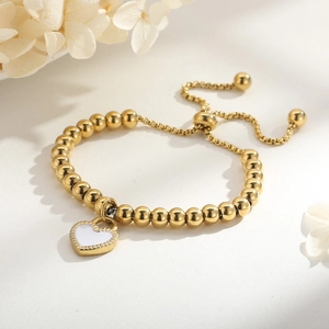 Détail du bracelet ajustable à billes dorées avec un pendentif cœur en émail blanc élégant