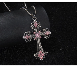 Detailed close-up of hip hop cross pendant with pink crystals on black textured background