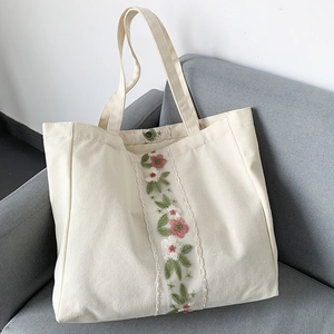 Dettaglio di ricamo e pizzo su una borsa tote in tela color crema su un divano