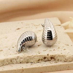 Silver teardrop earrings with grooved texture on stone pedestal in modern minimalist style