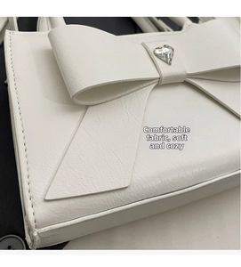 Detailed macro view of white leather handbag with oversized bow and heart rhinestone