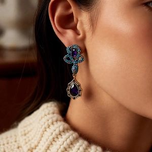 Detail of vintage teardrop earrings with purple stones on a model in beige knitwear